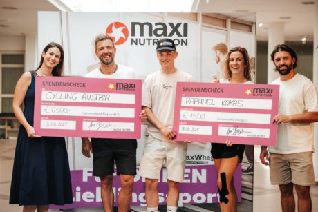 Der Gewinner der zweiten MaxiNutrition Sportchallenge Raphael Kokas hält die beiden Schecks mit seinen Teamkolleg:innen während der Siegerehrung.
