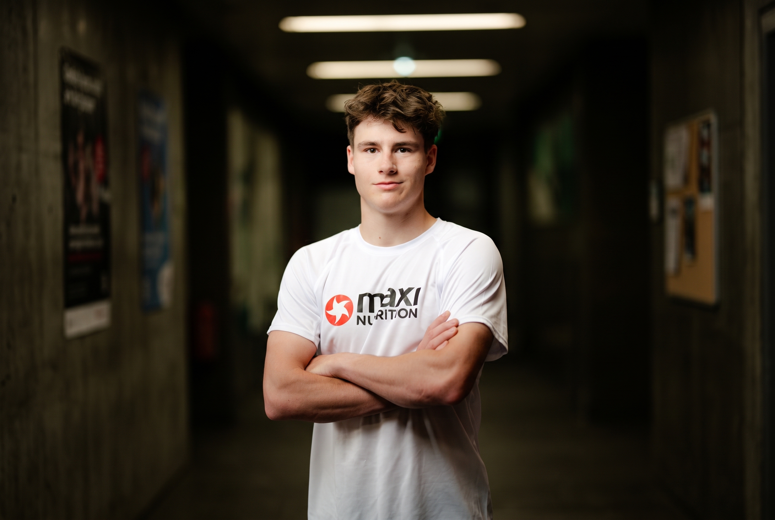 Elias trägt ein Kurzamshirt und hat die Arme vor der Brust verschränkt. Er hat kurze Haare und lächelt mit geschlossenen Lippen in die Kamera.