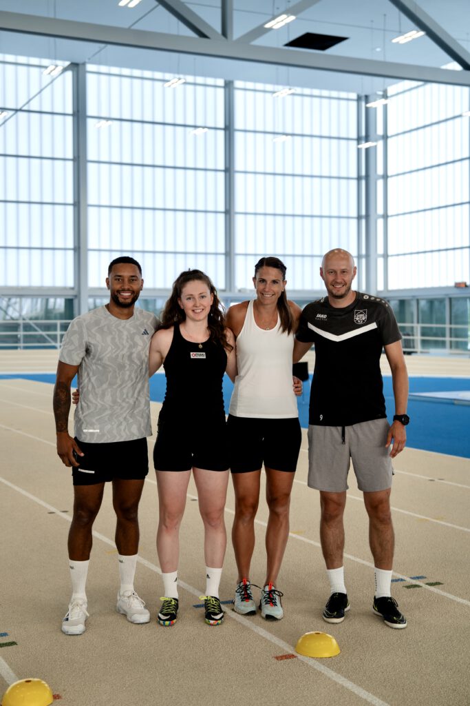Influencer Michael Blauensteiner, Nachwuchstalent Angelika Dallhammer, Skifahrerin Mirjam Puchner und Thomas Stütz stehen auf einer Laufbahn, halten sich in den Armen und lächeln in die Kamera für ein Gruppenbild.