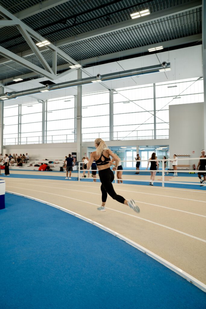 Ivona Dadic von hinten, wie sie um die Kurve der Laubahn sprintet. Sie trägt einen schwarzen Sport-BH und eine lange Sport-Leggings und einen Zopf.
