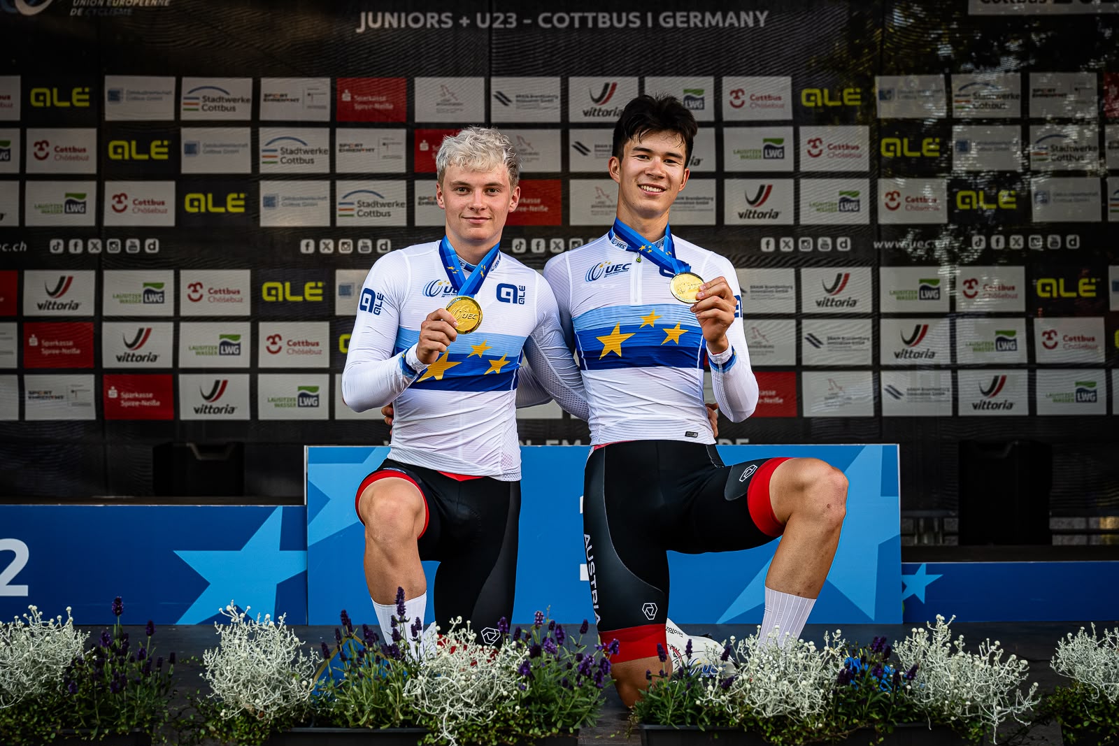 Raphael Kokas steht gemeinsam mit seinem Teamkollegen auf der Bühne und hat eine Goldmedaille in der Hand.